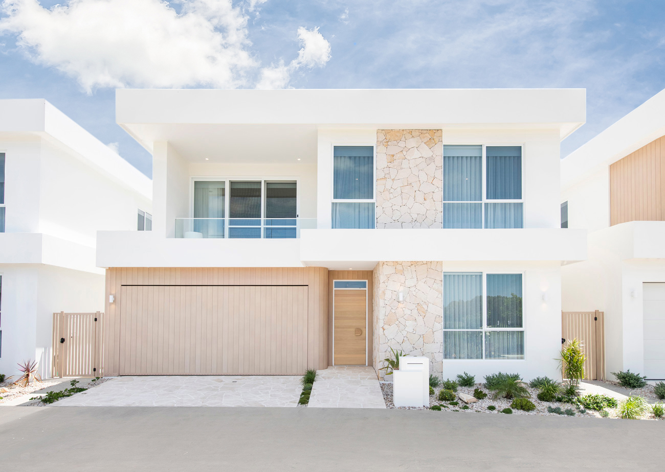 Bright, modern open-plan living space featuring a neutral-toned lounge area, a dining table with wicker chairs, and a white kitchen with an island and bar stools, styled with natural textures and minimalist décor.